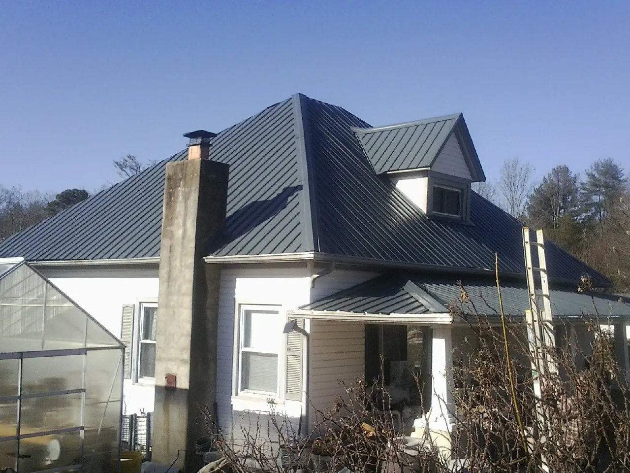Dark blue standing seam metal roof on a white farmhouse with dormer in Chicago Ridge