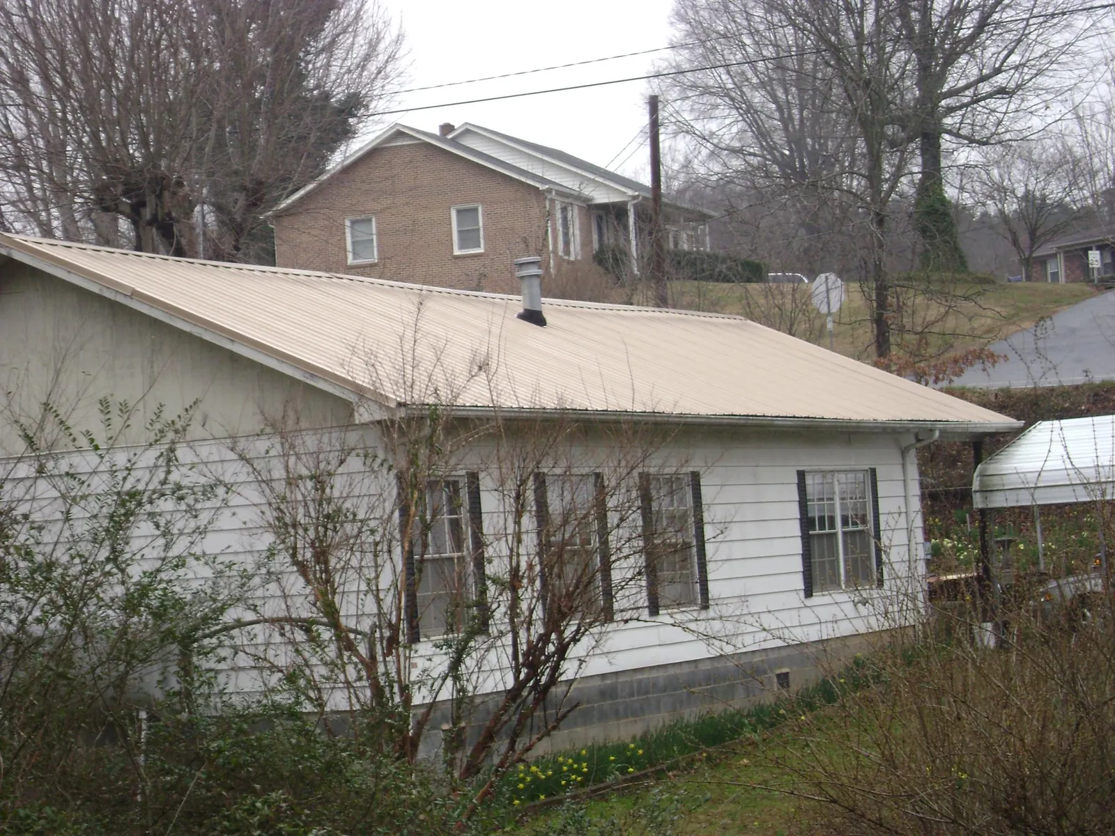 Tan metal roof on a white sided house set into a hillside — Commercial Roofing by Roofing Brothers in Chicago Ridge